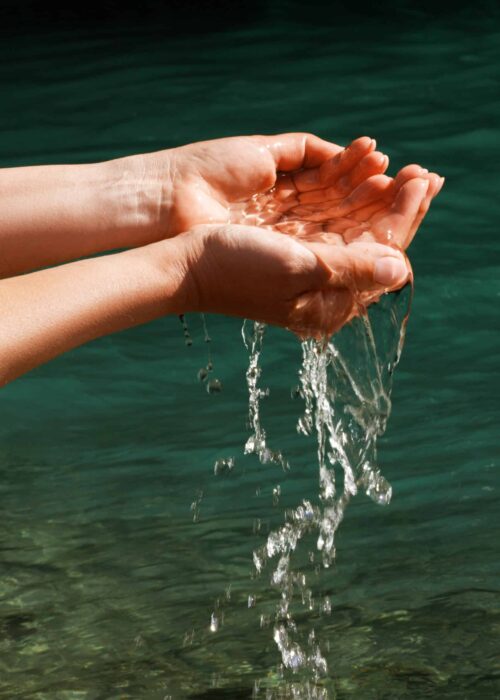 Women's hands, water is pouring near a river, sea, ocean. People in nature. Ecology. A woman touches the water with her hands.